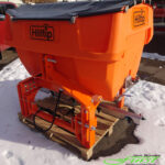 HILLTIP IceStriker 600TR in der Farboption Kommunal-Orange ausgestattet mit der Feuchtsalz-Vorbfeuchterbaugruppe, dem Solesprühbalken sowie dem Handsprühsystem sowie Kennzeichenbeleuchtungskit sowie Arbeitsscheinwerfer; geeignet für alle Traktoren und Zugmaschinen mit Dreipunktaufnahmen der Kategorien I, II und 0